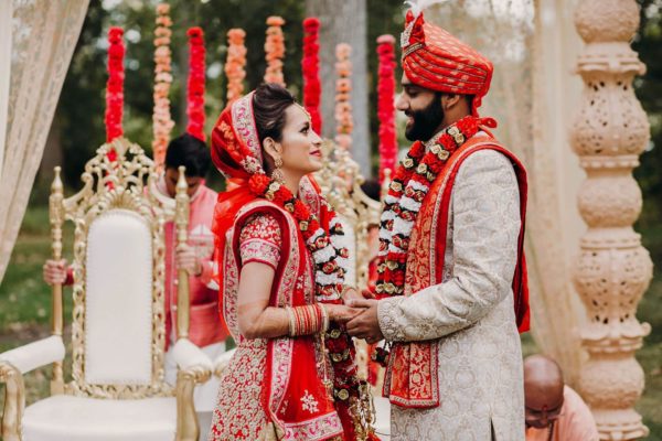 Indian bride and groom holding hands in wedding clothes.